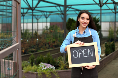 Female business owner holding OPEN sign in greenhouse. Space for text