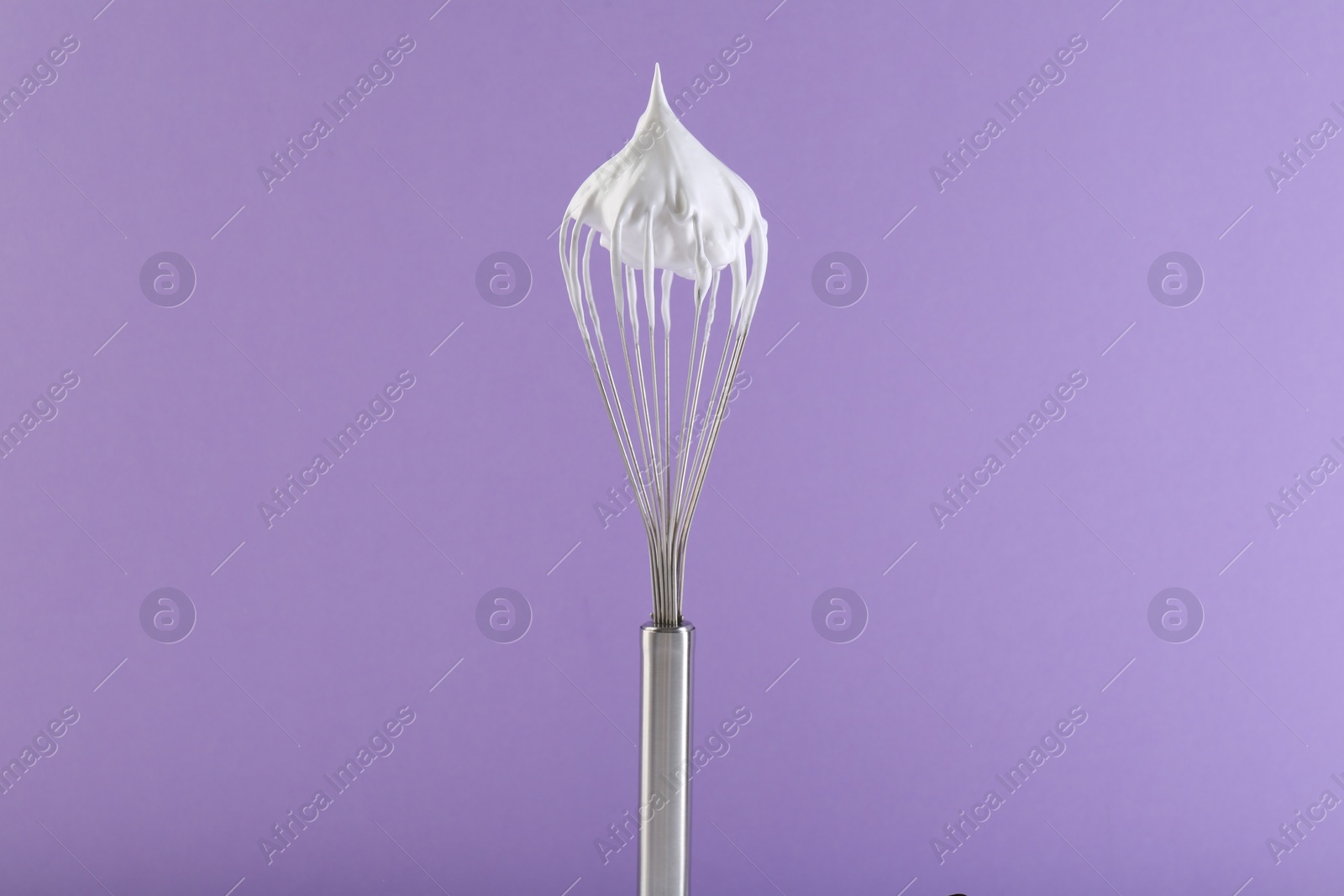 Photo of Whisk with whipped cream on violet background