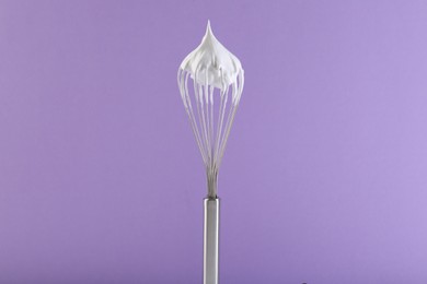 Photo of Whisk with whipped cream on violet background