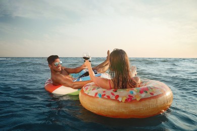 Photo of Couple with glasses of wine and inflatable rings in sea