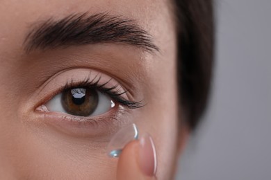 Photo of Closeup view of young woman putting in contact lens on grey background