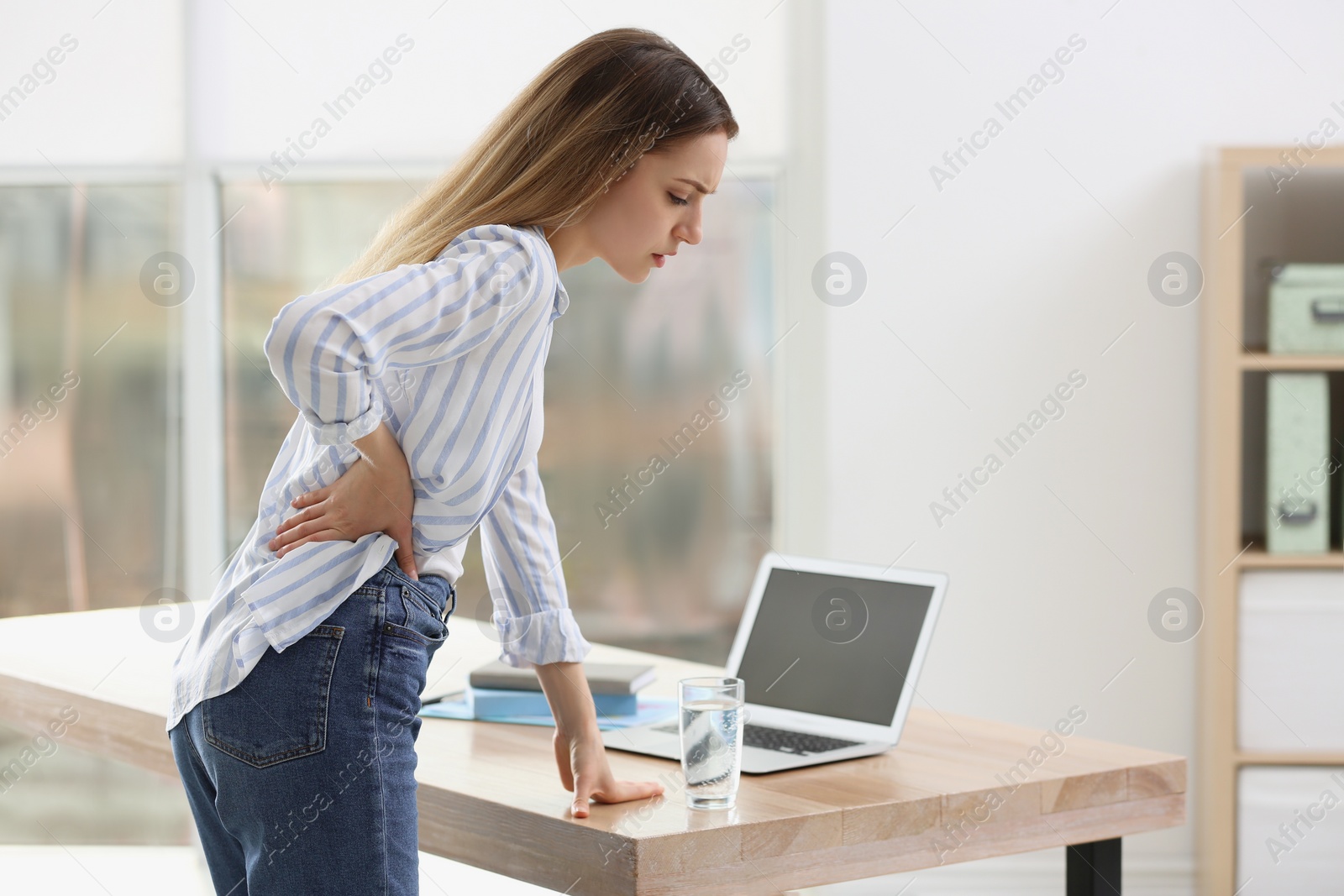 Photo of Woman suffering from back pain in office. Symptom of bad posture