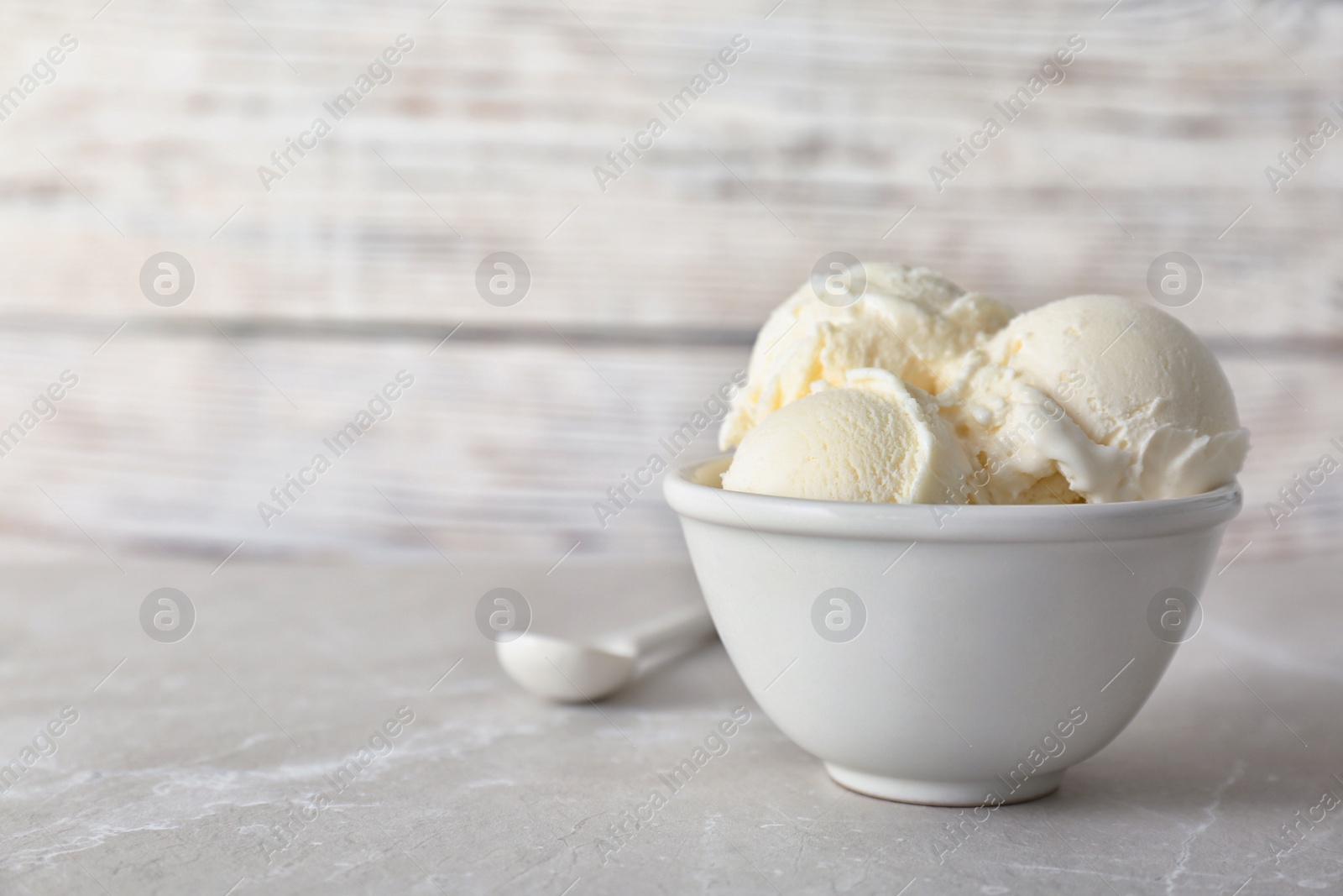 Photo of Bowl with tasty vanilla ice cream on table against light background