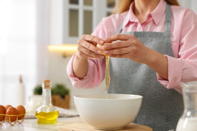 Photo of Making bread. Woman putting raw egg into bowl at white table in kitchen, closeup
