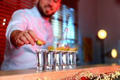 Photo of Barman putting lime on shot glass of Mexican Tequila at bar counter, closeup