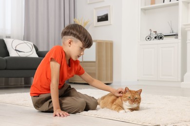 Photo of Little boy petting cute ginger cat on soft carpet at home