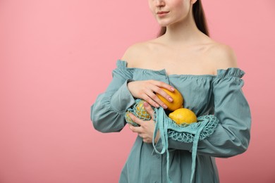 Photo of Woman with string bag of fresh lemons on pink background, closeup. Space for text