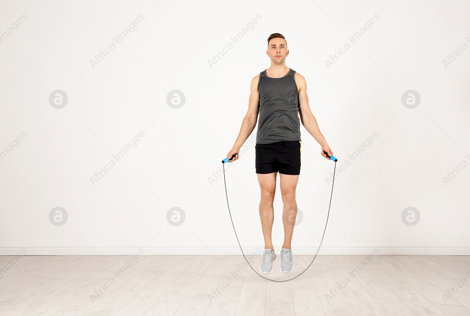 Photo of Full length portrait of young sportive man training with jump rope in light room