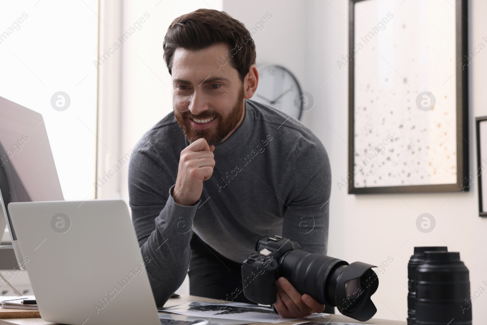 Photo of Professional photographer holding digital camera near table with laptop in office