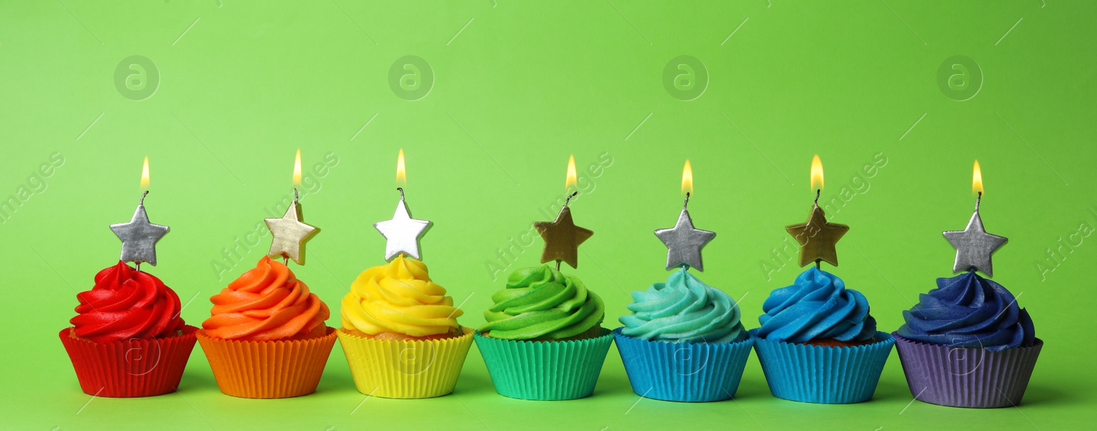 Photo of Delicious birthday cupcakes with burning candles on green background