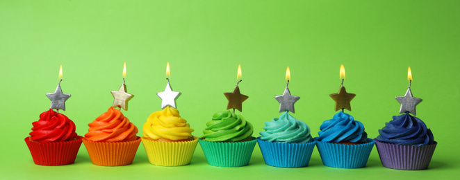 Photo of Delicious birthday cupcakes with burning candles on green background