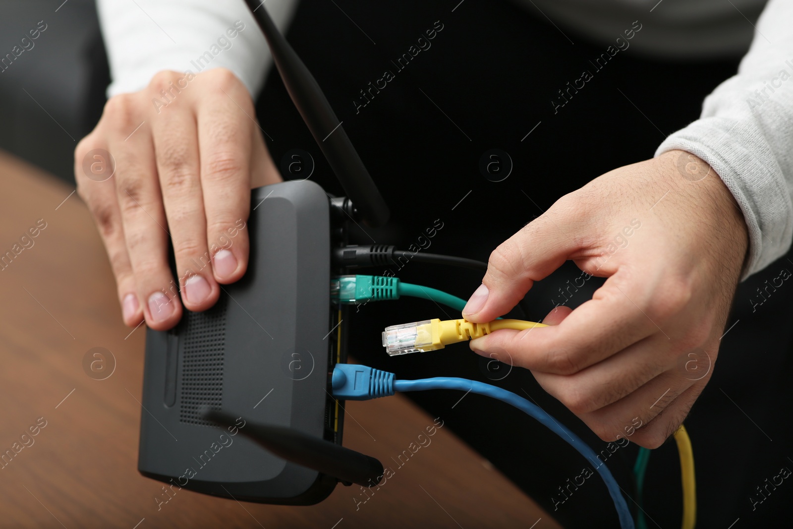 Photo of Man inserting cable into Wi-Fi router at wooden table indoors, closeup