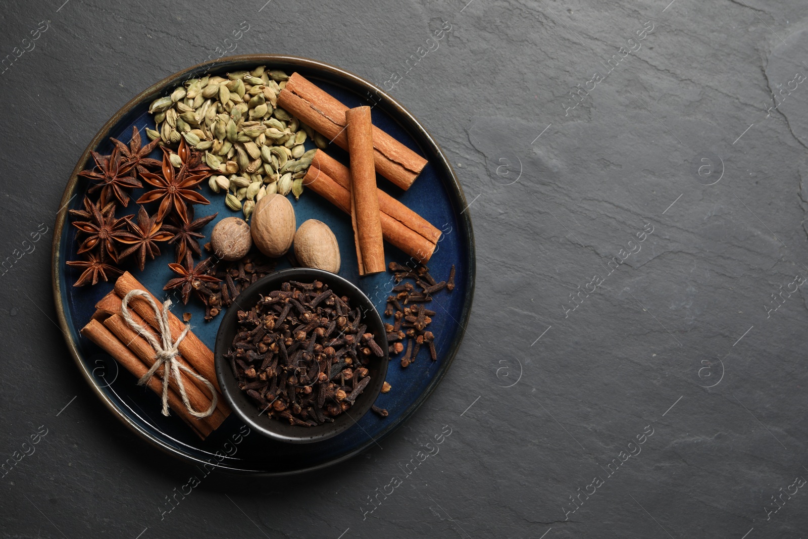 Photo of Dishware with different spices and nuts on gray table, top view. Space for text