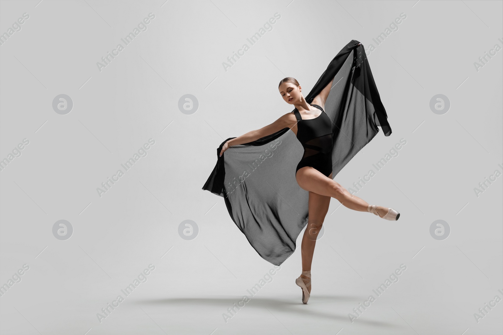 Photo of Graceful young ballerina practicing dance moves with black veil on light grey background. Space for text