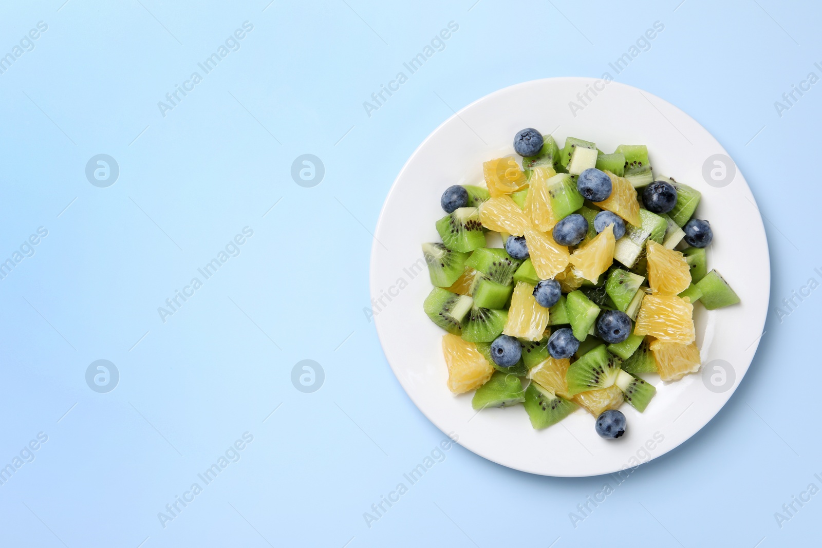 Photo of Plate of tasty fruit salad on light blue background, top view. Space for text