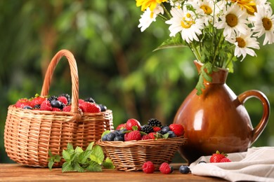 Photo of Different fresh ripe berries and beautiful flowers on wooden table outdoors