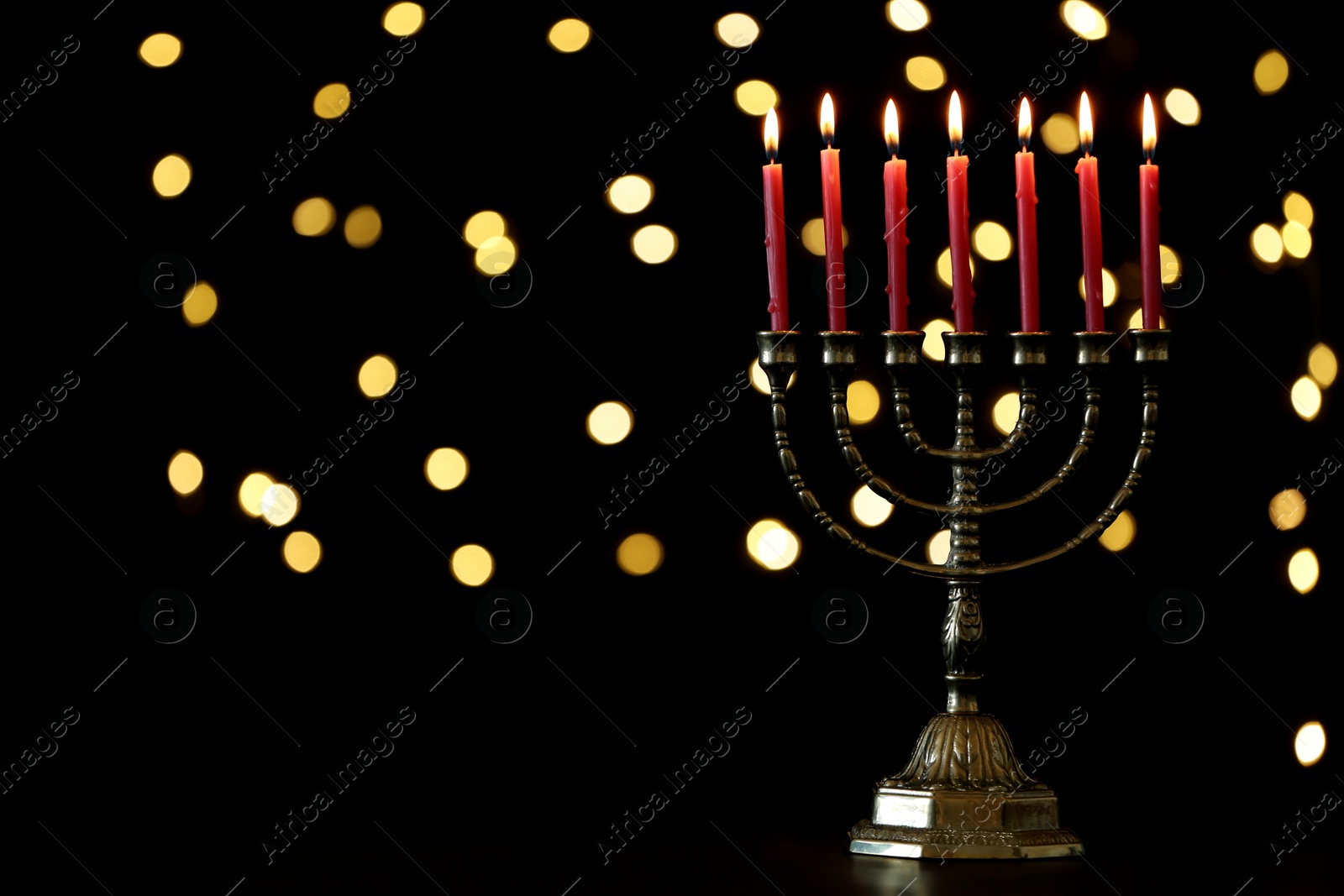 Photo of Golden menorah with burning candles against dark background and blurred festive lights, space for text