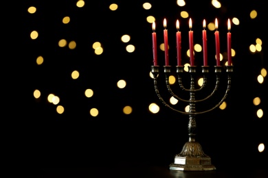 Photo of Golden menorah with burning candles against dark background and blurred festive lights, space for text