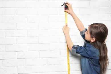 Photo of Little girl measuring her height on brick wall background