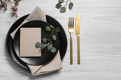 Stylish table setting with cutlery, blank card and eucalyptus leaves, flat lay. Space for text