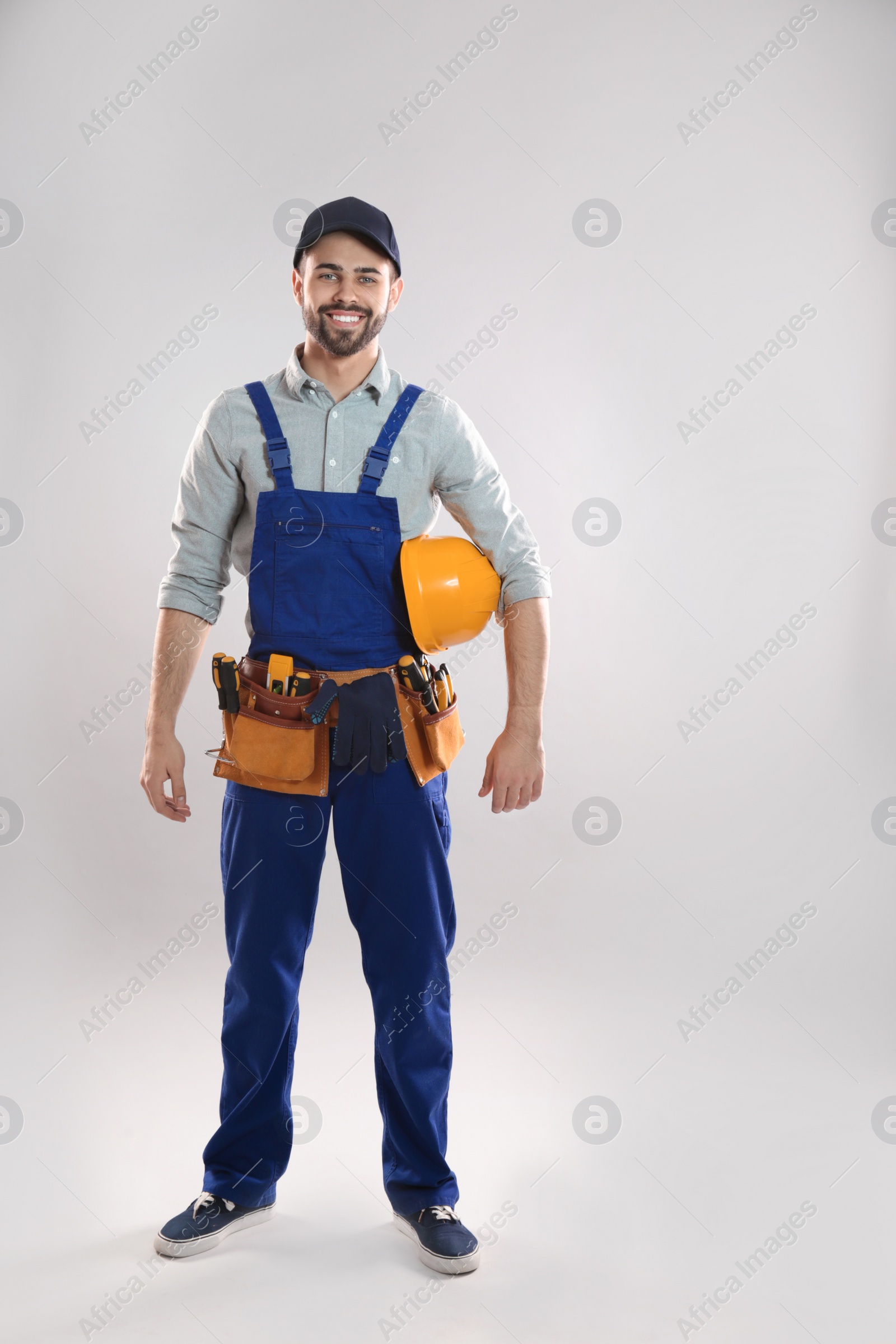 Photo of Full length portrait of construction worker with hard hat and tool belt on light background