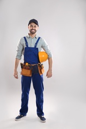 Photo of Full length portrait of construction worker with hard hat and tool belt on light background