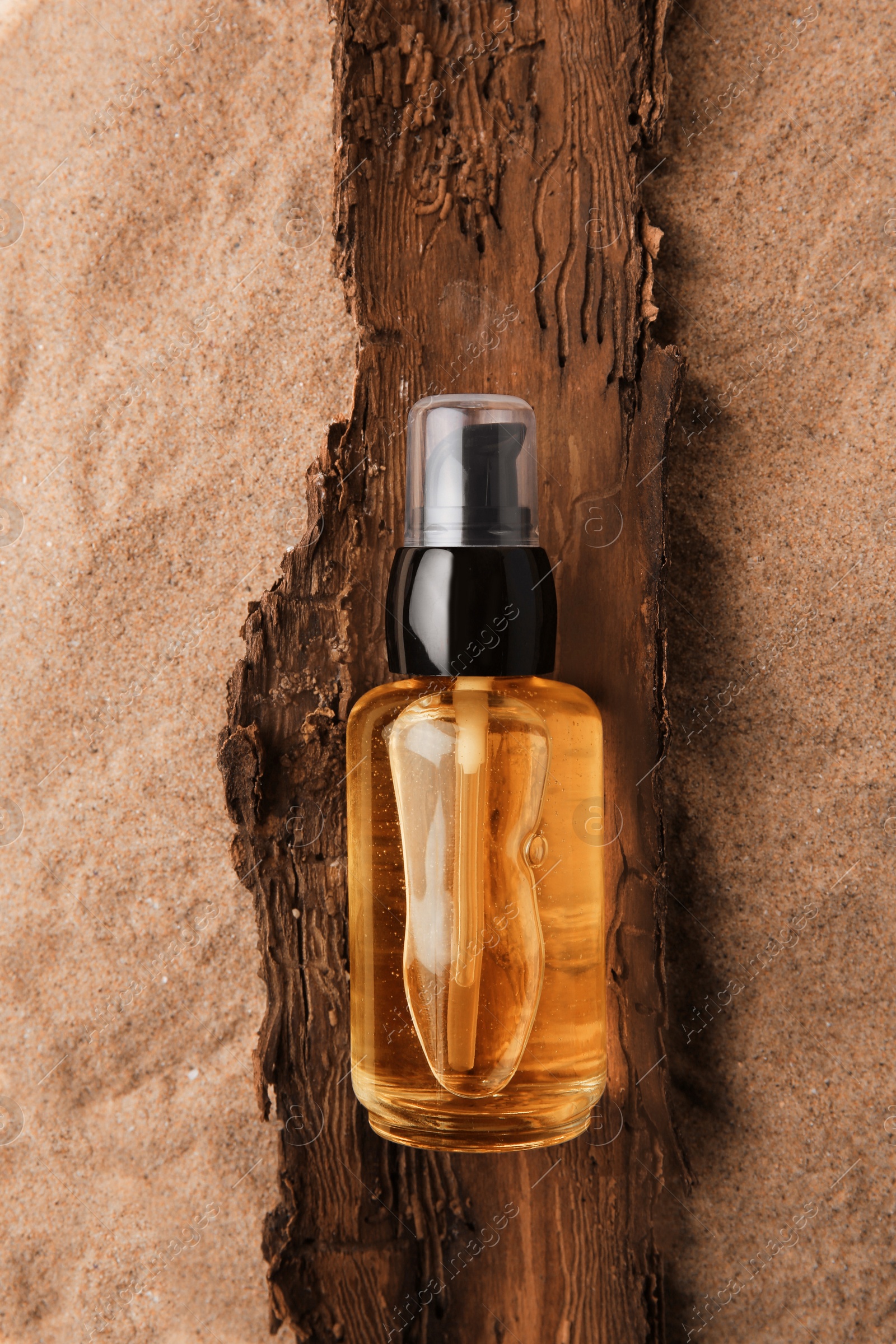 Photo of Bottle of serum and tree bark on sand against beige background, top view