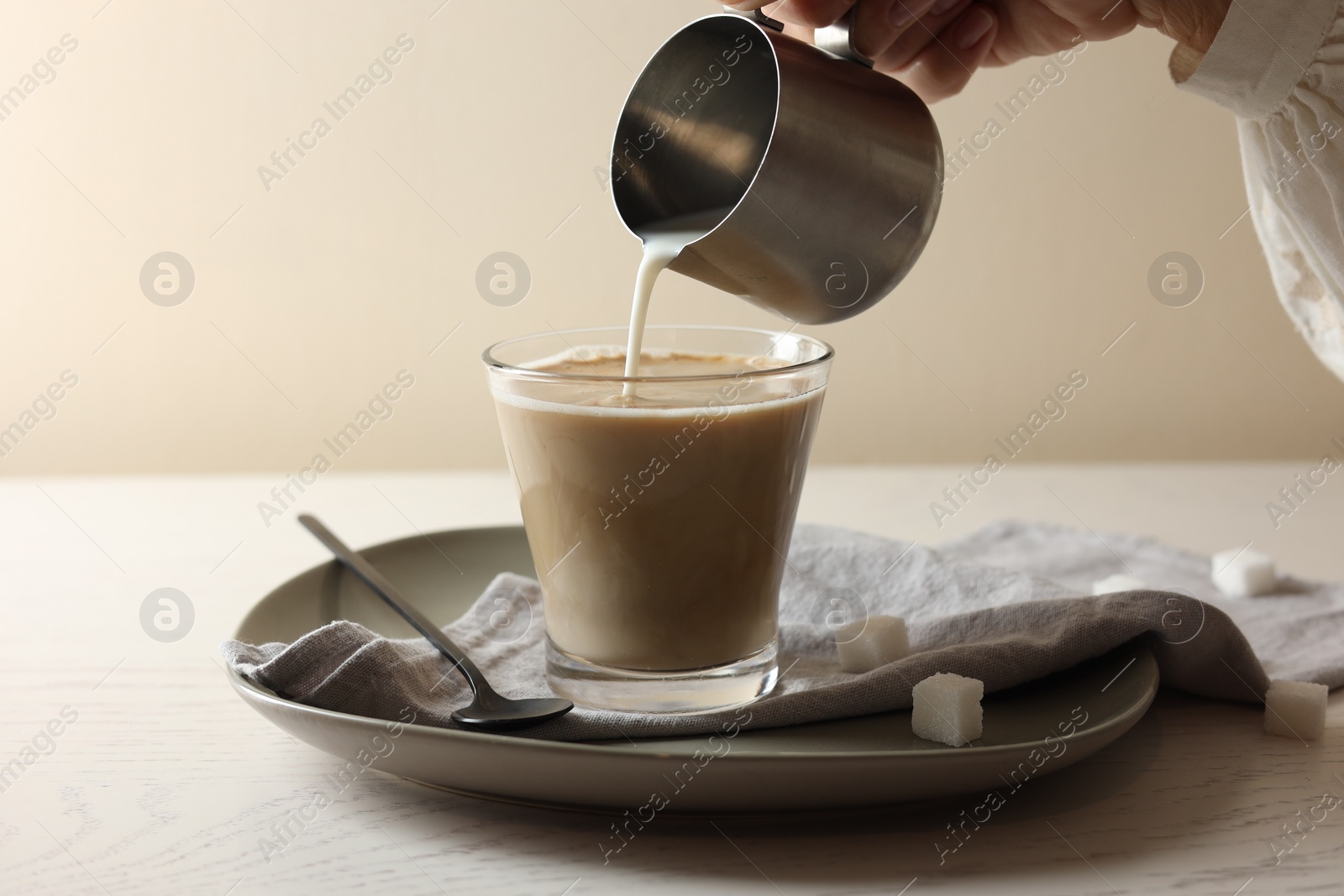 Photo of Pouring milk into cup with coffee on white wooden table, closeup