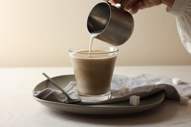 Pouring milk into cup with coffee on white wooden table, closeup