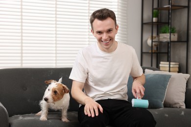 Pet shedding. Smiling man with lint roller removing dog's hair from pants at home