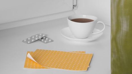 Photo of Pepper plasters, pills and cup with hot drink on window sill indoors