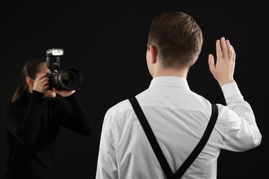 Photo of Professional photographer taking picture of man on black background, selective focus