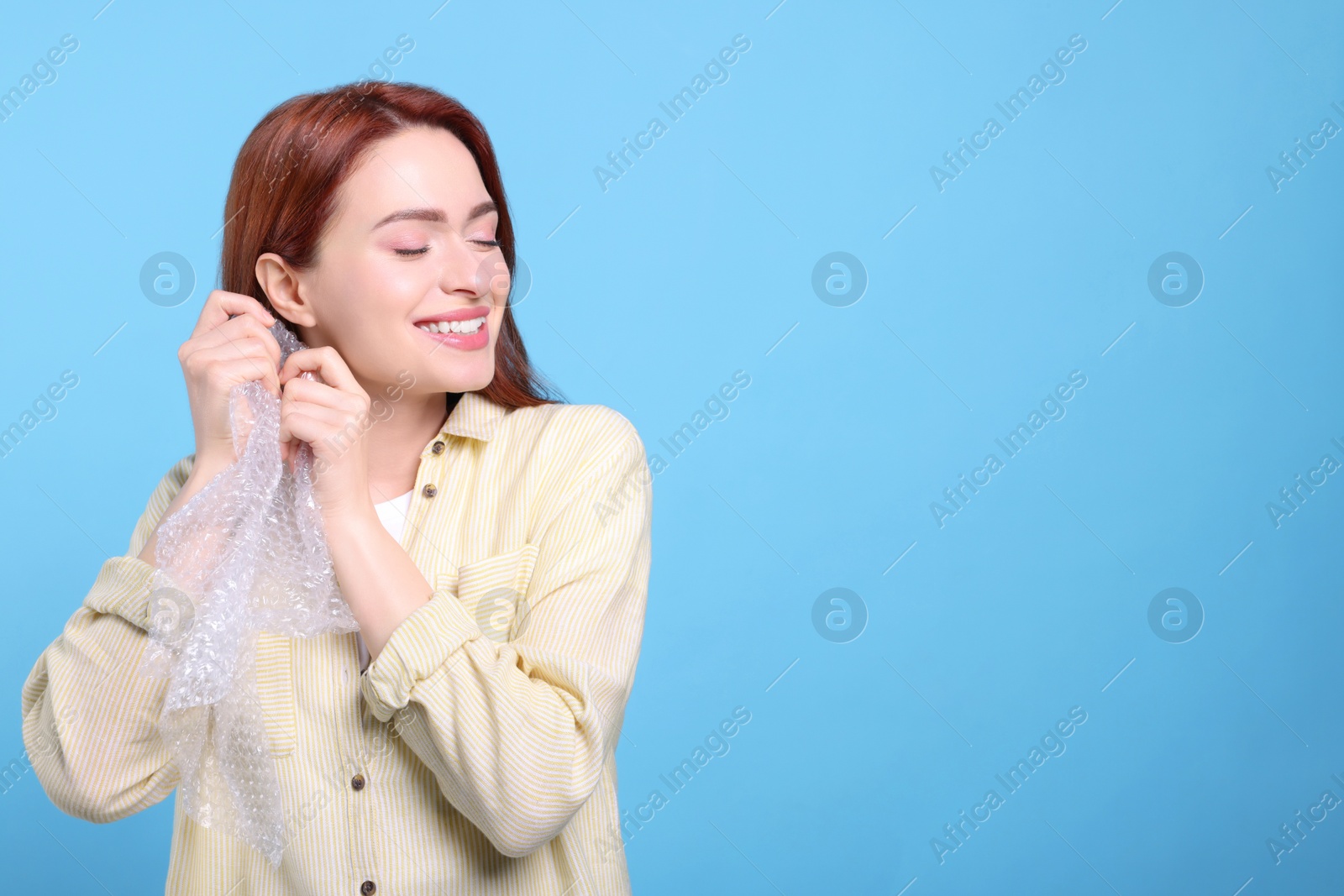 Photo of Woman popping bubble wrap on turquoise background, space for text. Stress relief