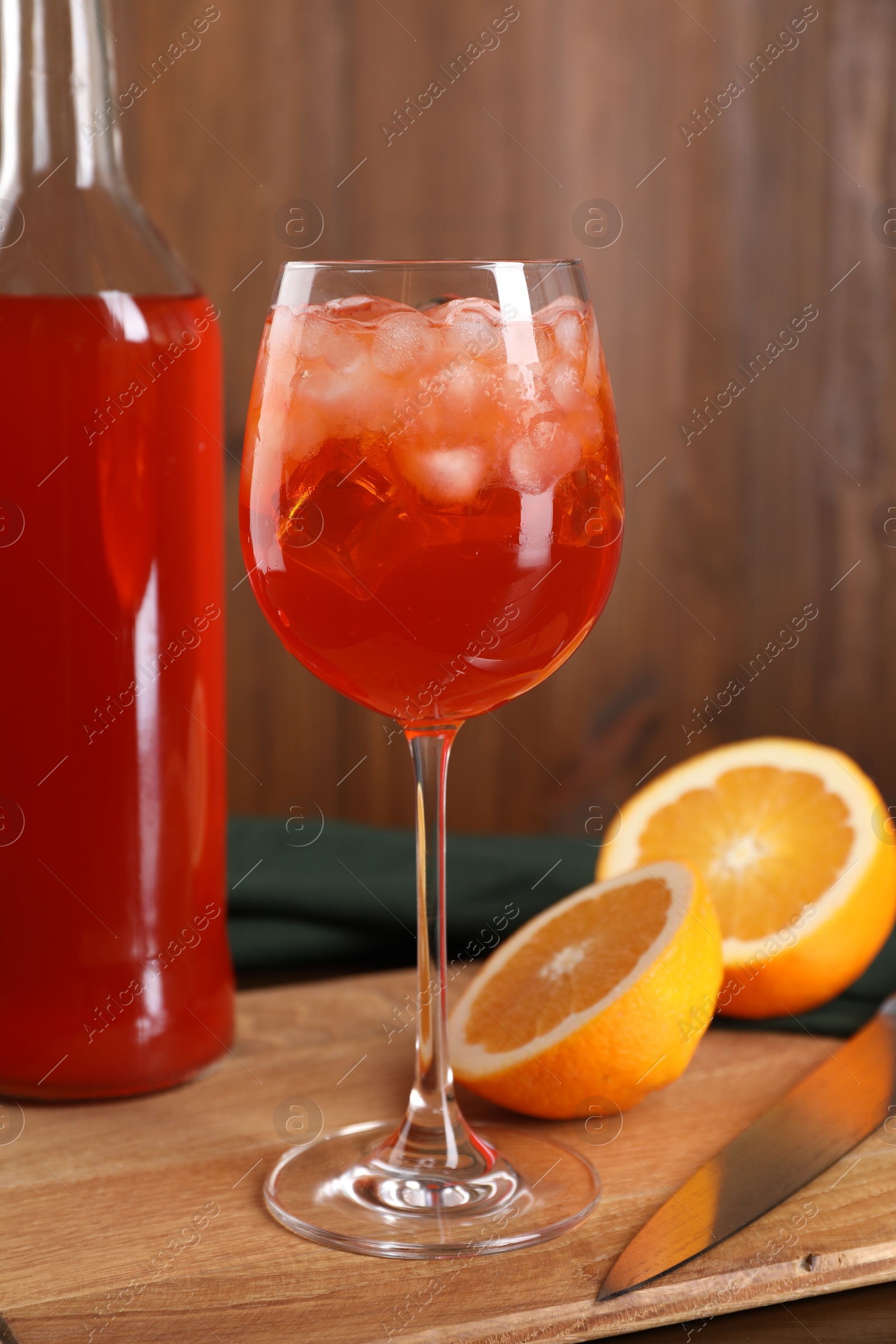 Photo of Aperol spritz cocktail and ice cubes in glass and bottle on wooden table, closeup