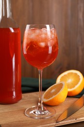 Aperol spritz cocktail and ice cubes in glass and bottle on wooden table, closeup