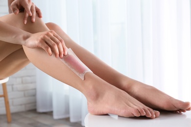 Woman doing leg epilation procedure with wax strips indoors, closeup