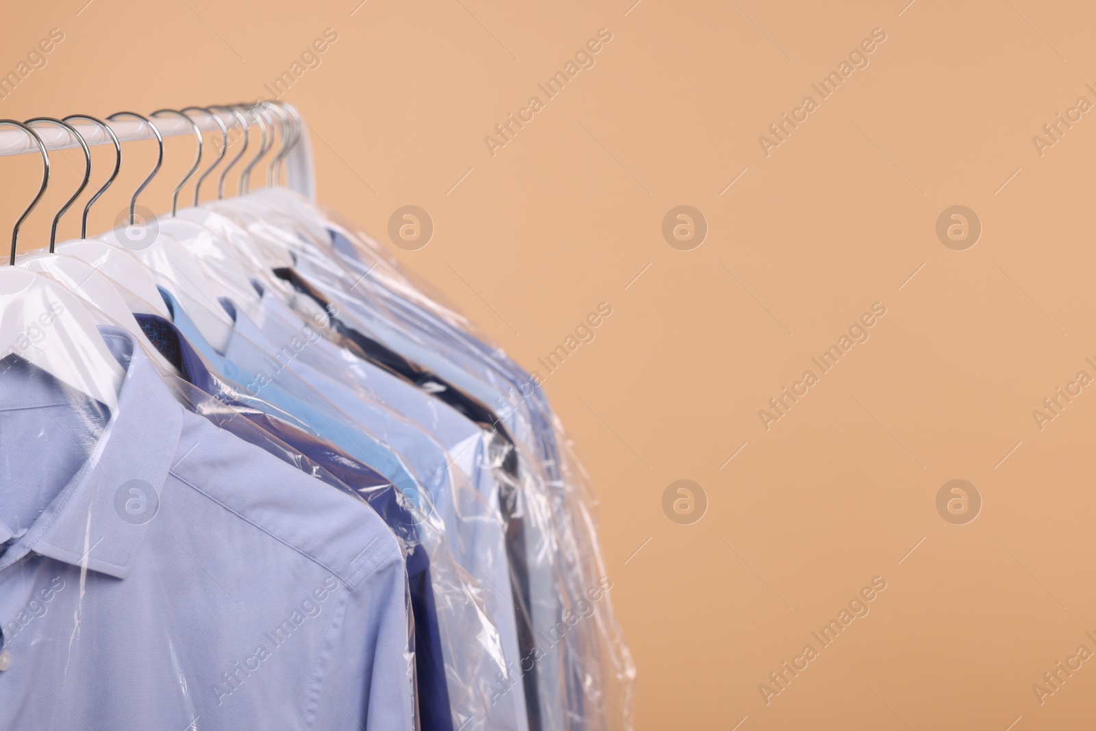 Photo of Dry-cleaning service. Many different clothes in plastic bags hanging on rack against beige background, space for text