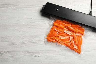 Photo of Vacuum packing sealer and plastic bag with cut carrots on white wooden table. Space for text