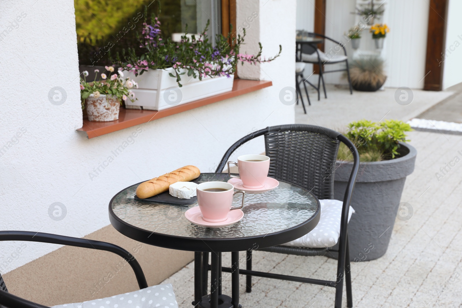 Photo of Cups of coffee, bread and cheese on glass table. Relaxing place at outdoor terrace