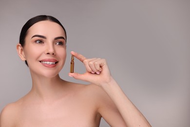 Photo of Beautiful young woman holding skincare ampoule on grey background. Space for text