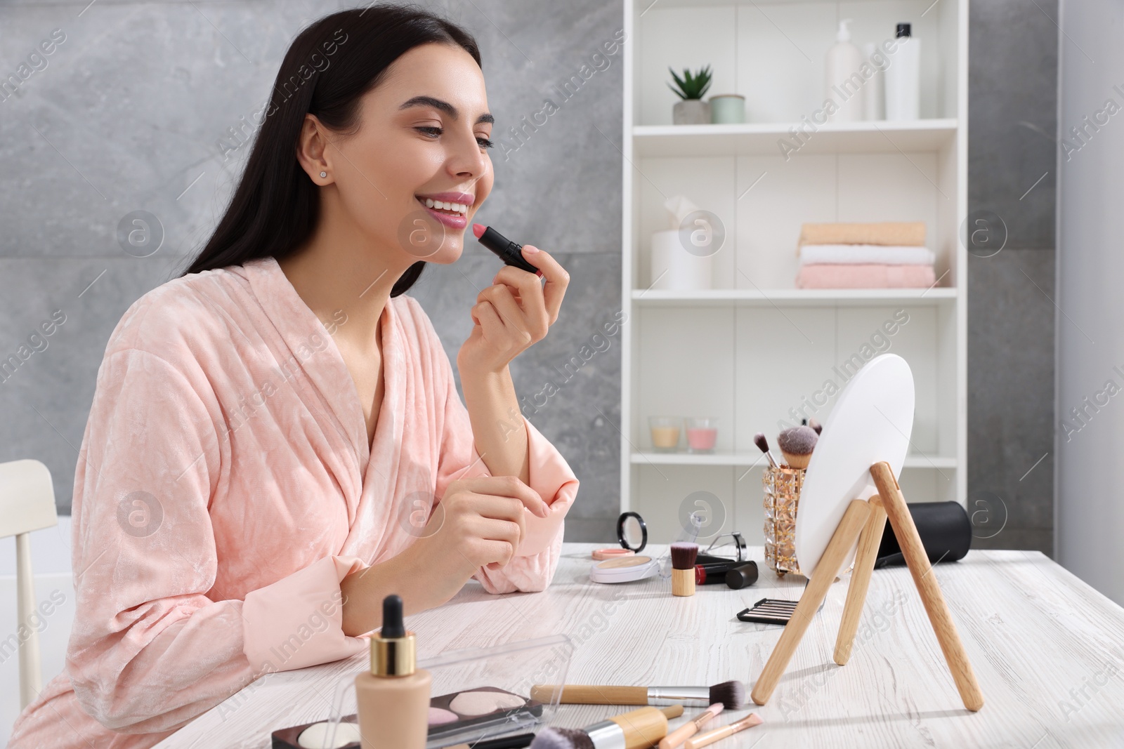 Photo of Beautiful young woman applying lipstick at dressing table indoors