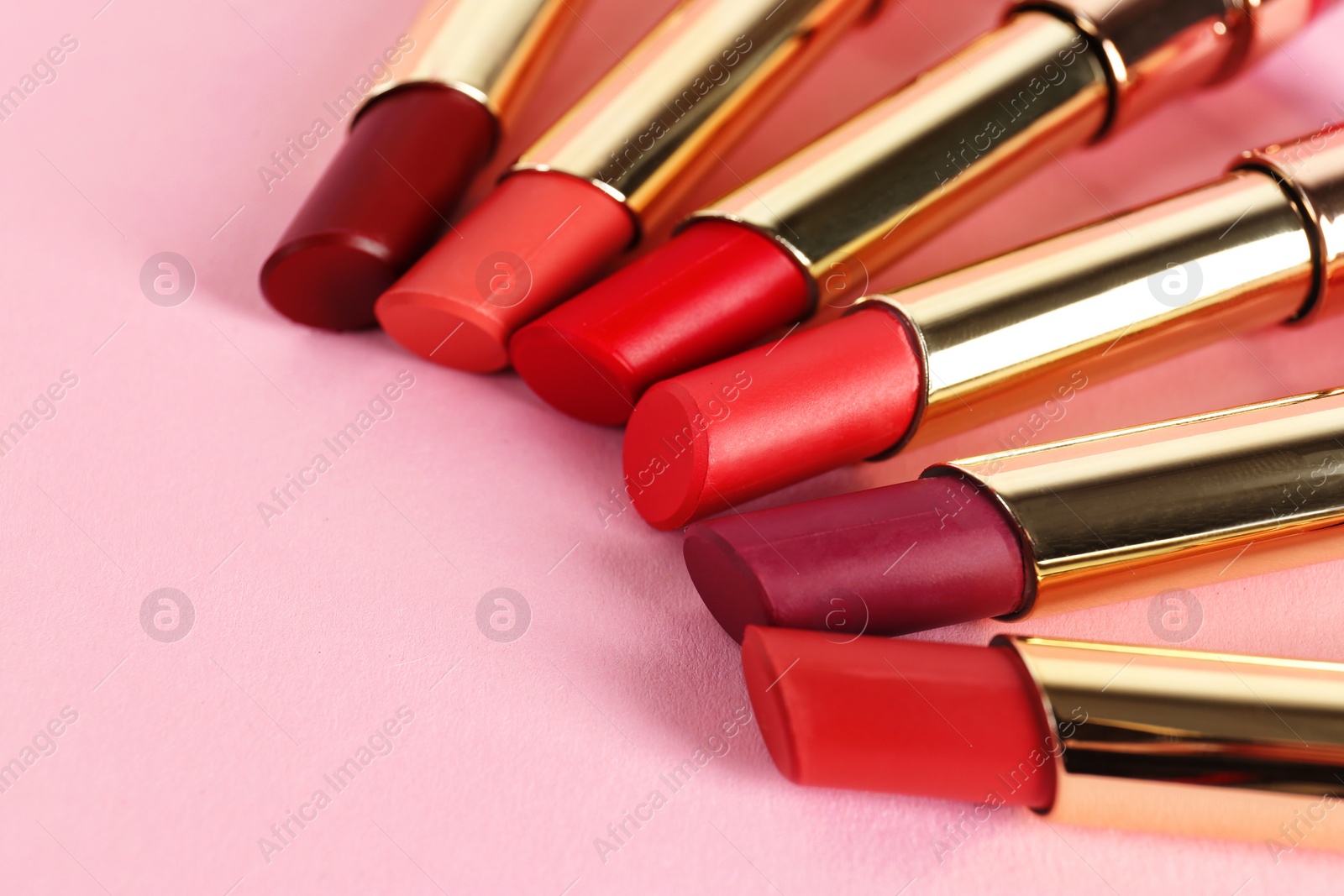 Photo of Set of bright lipsticks in gold tubes on pink background, space for text