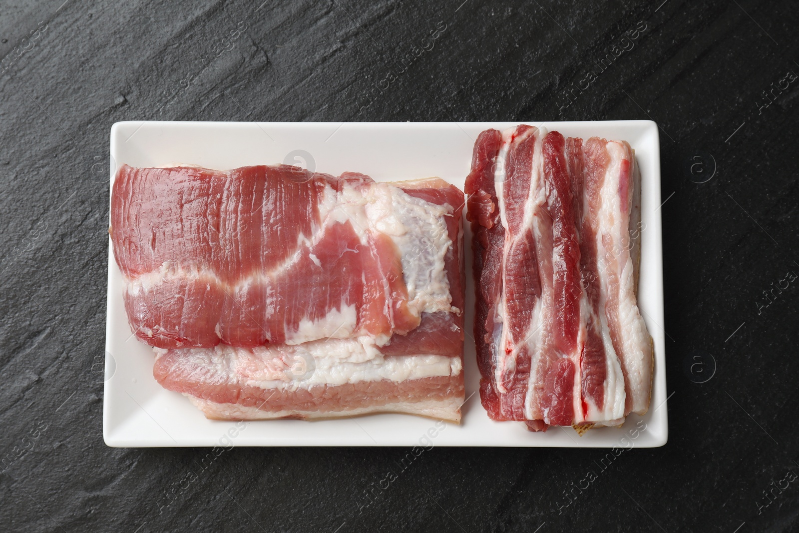 Photo of Pieces of raw pork belly on black textured table, top view