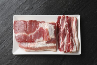 Pieces of raw pork belly on black textured table, top view