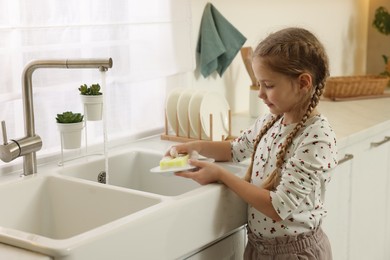 Photo of Little girl washing plate above sink in kitchen