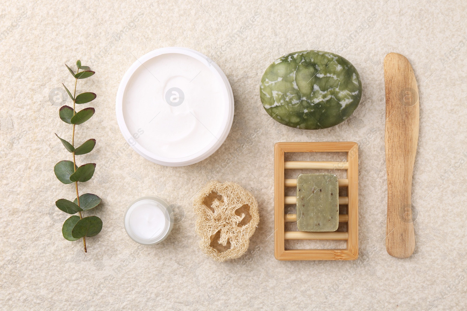 Photo of Flat lay composition with moisturizing cream in open jar and other body care products on light textured table