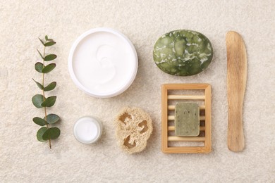 Photo of Flat lay composition with moisturizing cream in open jar and other body care products on light textured table