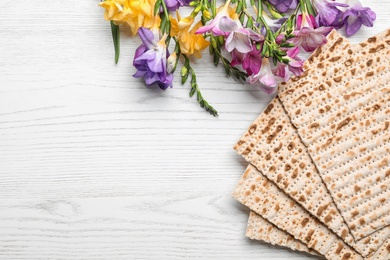 Photo of Flat lay composition of matzo and flowers on wooden background, space for text. Passover (Pesach) Seder