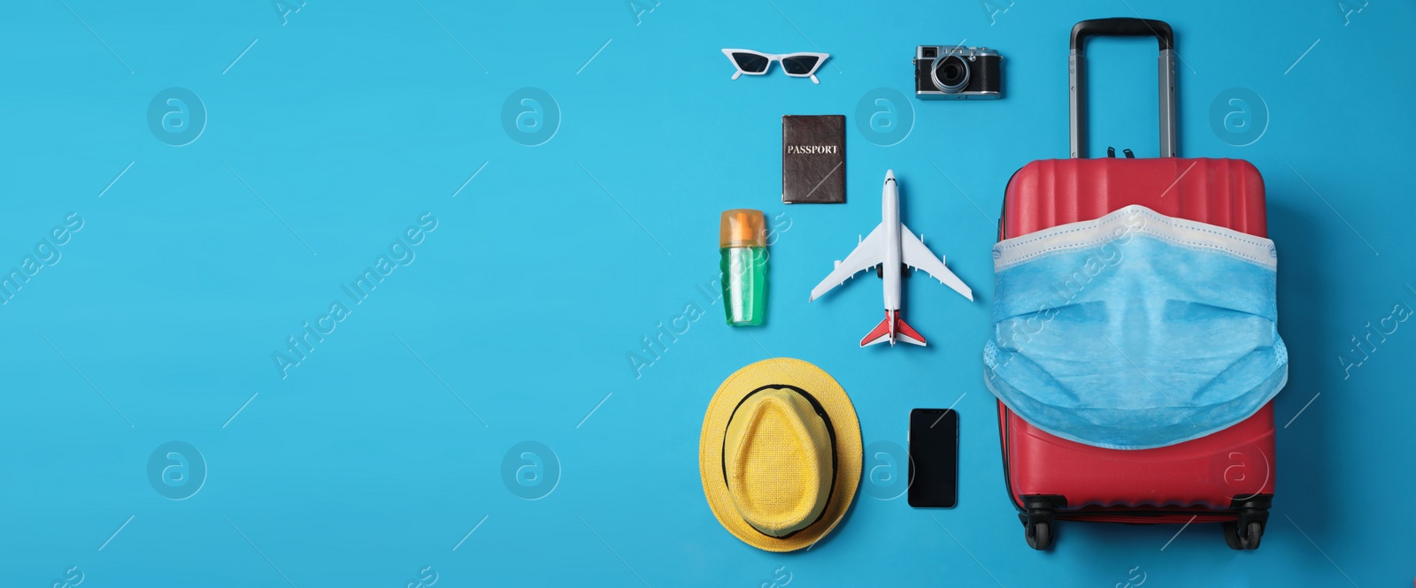 Image of COVID-19 pandemic, travel during coronavirus outbreak. Suitcase with protective mask and accessories on blue background, flat lay 