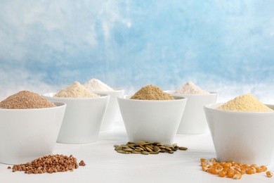 Photo of Bowls with different types of flour and seeds on table against color background. Space for text